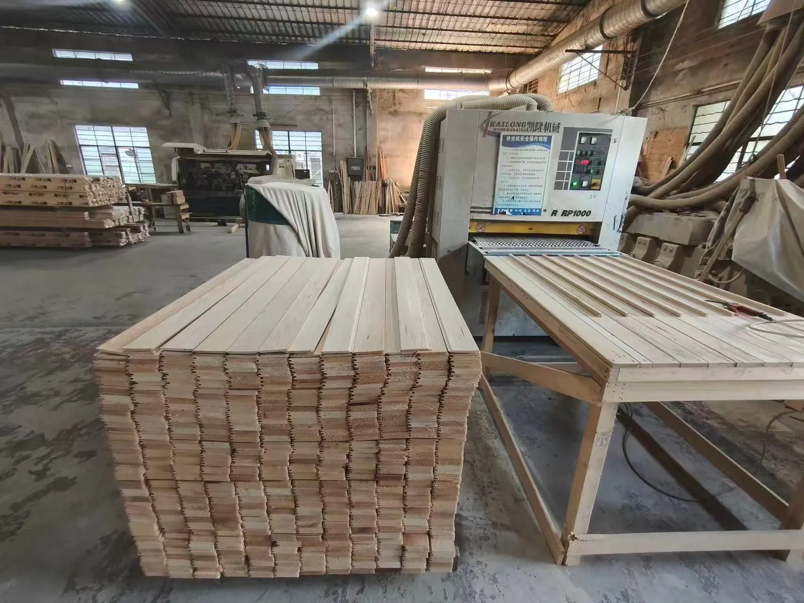 Stack of milled sauna panel boards beside the sanding line at the FENYA workshop